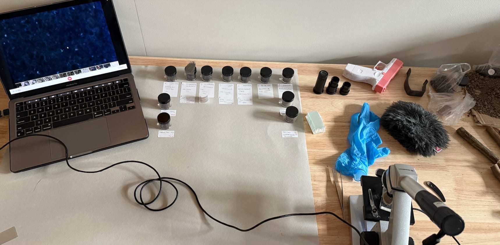 Studio setup with a microscope, soil samples in labelled jars, and a laptop showing microscope footage