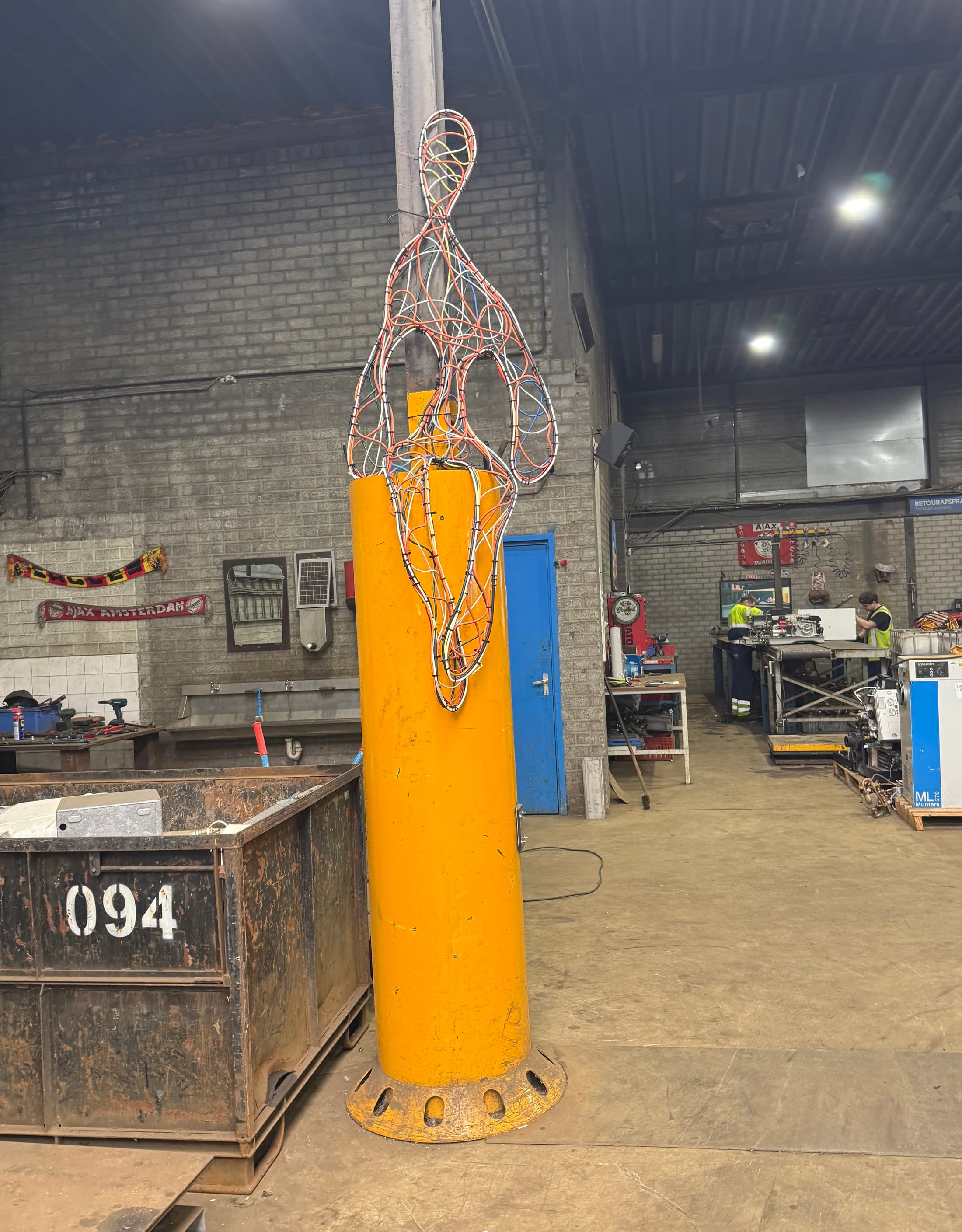 Cable Man sculpture on an orange industrial post at the e-waste facility