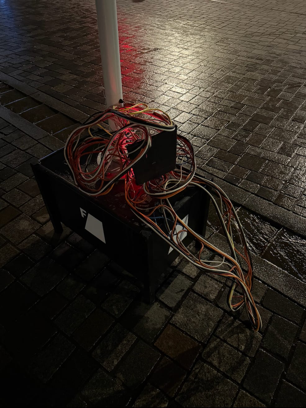 Cable Man glowing red at night, wrapped around a pole with a recycling bin